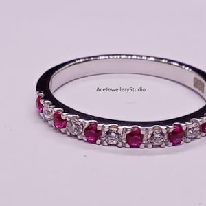 Può includere: Un anello d'argento con pietre preziose rosse e chiare alternate. L'anello è posto su uno sfondo bianco. Il testo "AceJewelleryStudio" è visibile sull'anello.