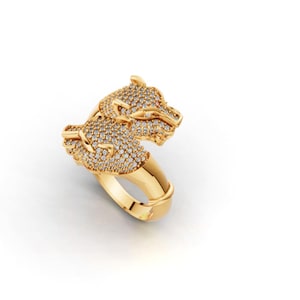 Könnte beinhalten: Ein goldfarbener Ring mit einem detaillierten Design von zwei Tierköpfen, möglicherweise Großkatzen, die mit kleinen, funkelnden Steinen besetzt sind. Der Ring hat einen dicken Ring und ein detailliertes, strukturiertes Aussehen.