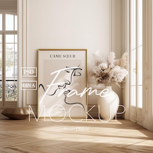 Puede incluir: Interior de una habitación con un gran cuadro enmarcado, un jarrón blanco con flores secas y un objeto decorativo dorado. El cuadro enmarcado tiene un marco dorado y presenta un dibujo lineal de dos caras con el texto "L'ÂME SOEUR".
