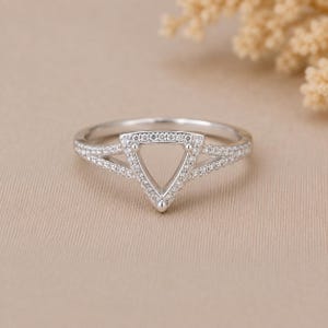 May include: A silver-toned ring featuring a central triangular frame encrusted with small clear stones. The band splits into two delicate arms that meet at the triangle, with both the band and the triangular setting covered in pavé-set stones.