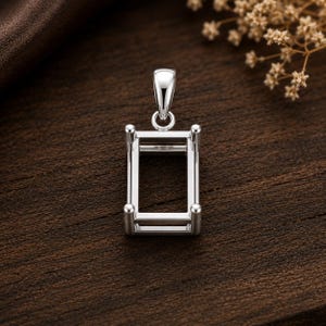 Peut inclure: Un pendentif en métal argenté composé d'un cadre rectangulaire avec quatre griffes verticales aux coins, conçu pour maintenir une pierre précieuse. Le support comprend une bélière polie sur le dessus pour l'attacher à une chaîne ou un cordon.
