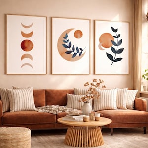 Pode incluir: Três impressões de arte abstrata emolduradas com um tema celestial. Cada impressão apresenta designs em estilo aquarela em tons de laranja, marrom e azul marinho. As impressões são exibidas acima de um sofá marrom com almofadas listradas.