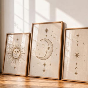 May include: Three framed celestial art prints. The prints feature a sun with a face, a crescent moon with a face, and a starburst design. The artwork is in shades of brown and beige, with wooden frames.