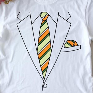 Könnte beinhalten: Weißes T-Shirt mit einem grafischen Design eines Anzugs, einer Krawatte und einem Einstecktuch. Die Krawatte hat orange und grüne Streifen. Das Einstecktuch hat ein passendes Streifendesign. Ein lässiges Kleidungsstück.