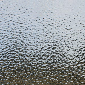 May include: Close-up of a textured glass surface. The glass has a pattern of small, irregular bumps, creating a unique visual effect. The texture is primarily silver and white, with subtle variations in light and shadow.