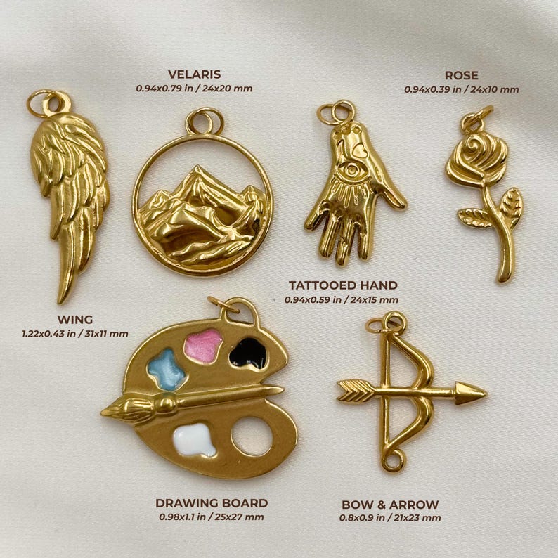 May include: A collection of gold-colored charms, including a wing, mountain scene, tattooed hand, rose, drawing board, and bow and arrow. Measurements are provided in inches and millimeters. The charms are designed for jewelry making or crafting.