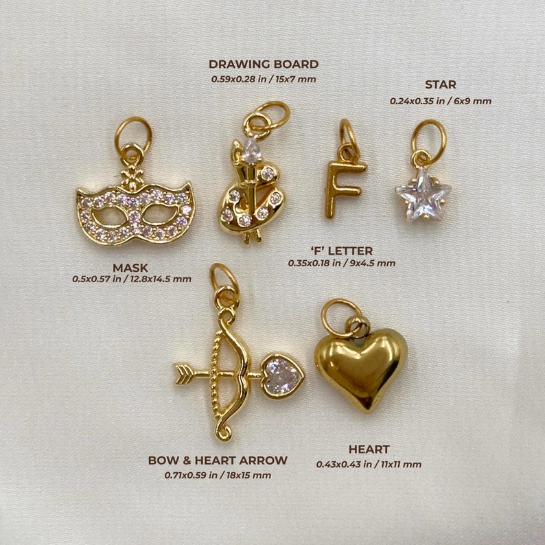 May include: A collection of gold-colored charms, including a mask, a bow and heart arrow, a heart, a star, an "F" letter, and a drawing board. The mask measures 0.5x0.57 inches, and the heart measures 0.43x0.43 inches. Each charm has a small loop for attachment.