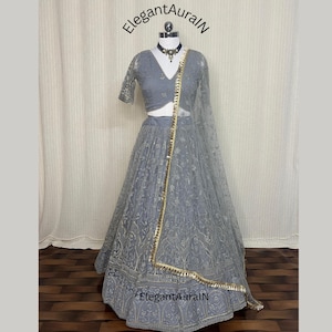 May include: A grey lehenga choli set on a mannequin, featuring a cropped top, full skirt, and sheer dupatta. The outfit is embroidered and trimmed with gold. The text "ElegantAuralN" is visible. Measurements are in centimeters.