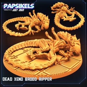 May include: A monochromatic orange miniature figure of a creature with an elongated head, sharp teeth, and a long segmented tail, displayed in three different poses. The text "PAPSIKELS JULY 2021" and "DEAD XENO BROOD RIPPER" is visible.