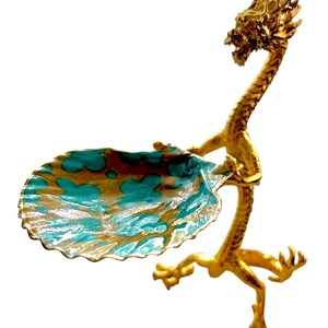 K&ouml;nnte beinhalten: Eine goldfarbene, drachenf&ouml;rmige Dekoschale mit einem t&uuml;rkis-goldenen Becken. Der Drachenkopf ist erhoben, und sein K&ouml;rper bildet die St&uuml;tze der Schale. Die Schale hat einen gewellten Rand.