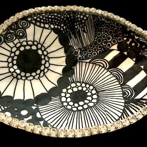 Peut inclure: Bol d&eacute;coratif ovale avec un motif floral noir et blanc. Le bord est bord&eacute; de petits strass &eacute;tincelants. L'int&eacute;rieur du bol pr&eacute;sente un design graphique audacieux avec des &eacute;l&eacute;ments circulaires et lin&eacute;aires.