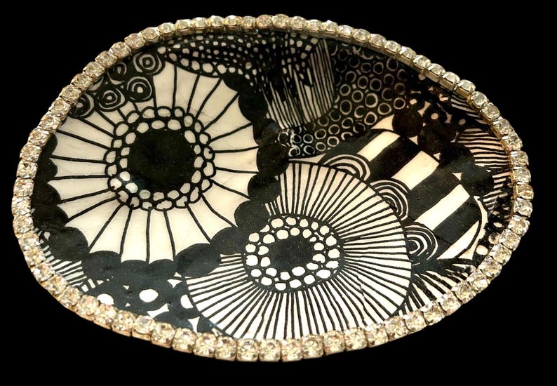 Peut inclure: Bol d&eacute;coratif ovale avec un motif floral noir et blanc. Le bord est bord&eacute; de petits strass &eacute;tincelants. L'int&eacute;rieur du bol pr&eacute;sente un design graphique audacieux avec des &eacute;l&eacute;ments circulaires et lin&eacute;aires.