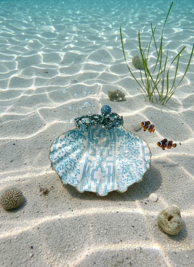 May include: An ornate seashell with a blue and white geometric design, topped with a beaded crown and a blue jewel. The underwater scene includes two clownfish. The shell sits on a sandy seabed, with a few plants.