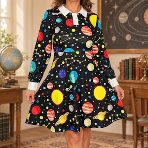 May include: A black long-sleeve dress featuring a colorful space-themed print of planets, stars, and constellations. The dress has a white pointed collar and white cuffs on the sleeves, with a button-down placket at the neckline.