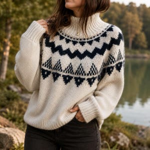 May include: A cream-colored knit sweater featuring a high mock neck and long sleeves. The garment displays a dark navy blue geometric pattern across the chest and shoulders, consisting of repeating zigzag lines and triangular shapes in a knit texture.