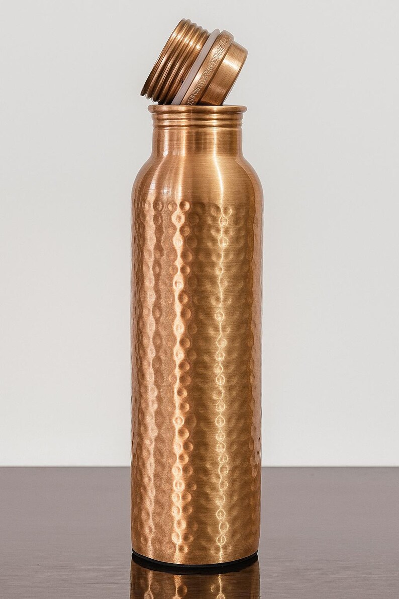 May include: A copper-colored water bottle with a textured, hammered finish. The bottle has a screw-on lid that is partially unscrewed. The bottle is cylindrical and has a capacity of approximately 25 ounces.