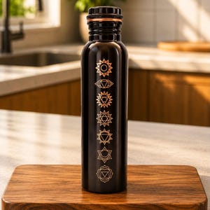 K&ouml;nnte beinhalten: Eine schwarze, zylindrische Wasserflasche mit sieben vertikal angeordneten, kupferfarbenen Chakra-Symbolen. Die Flasche hat eine glatte Oberfl&auml;che und einen metallisch kupferfarbenen Rand am Schraubverschluss, der ebenfalls schwarz und geriffelt ist.