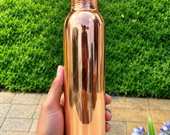 Puede incluir: Una botella de agua de cobre pulido con un cuerpo cilíndrico liso y reflectante y una tapa de rosca a juego. La superficie metálica presenta un tono marrón rojizo cálido, mostrando un diseño limpio con un cuello estrecho y tapa.