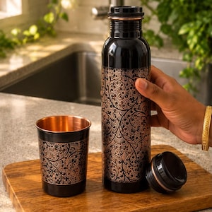 K&ouml;nnte beinhalten: Eine schwarze Metallwasserflasche und ein passender Trinkbecher, beide mit einem komplizierten kupferfarbenen Blumenmuster versehen. Die Flasche hat einen abnehmbaren schwarzen Schraubverschluss und das Innere des Bechers zeigt ein poliertes Kupfer-Finish.