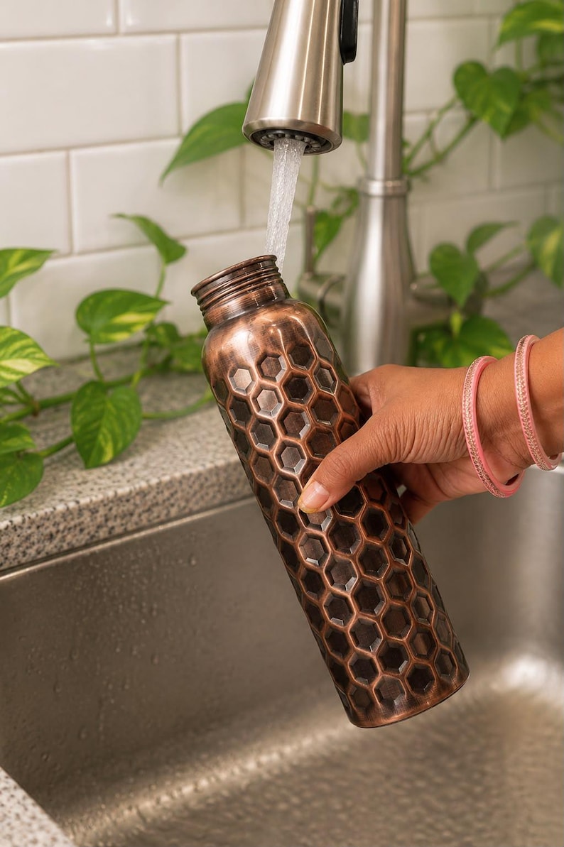 K&ouml;nnte beinhalten: Eine zylindrische Wasserflasche aus Kupfer mit einem erhabenen, sechseckigen Wabenmuster auf der Au&szlig;enfl&auml;che. Die Flasche hat einen schmalen Hals mit einem Gewindeverschluss und eine dunkle, br&uuml;nierte Metalloberfl&auml;che mit hellen Akzenten.