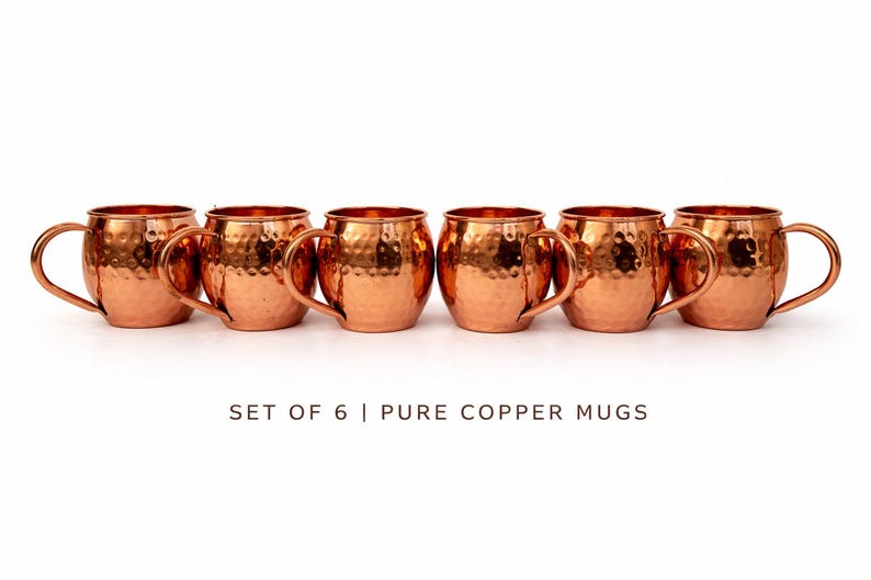 May include: Set of six pure copper mugs with a hammered finish. Each mug has a rounded body, a curved handle, and a bright copper color. The mugs are arranged in a row against a white background.