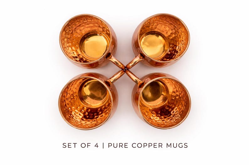 May include: Four copper mugs with a hammered texture, arranged in a cross shape against a white background. The mugs have a shiny, golden interior and small handles. The text at the bottom reads "SET OF 4 | PURE COPPER MUGS".
