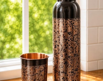 May include: A dark copper water bottle and a matching cup, both featuring an intricate, etched floral pattern in a contrasting metallic copper finish. The bottle has a cylindrical body with a rounded cap, while the cup is a simple tumbler.