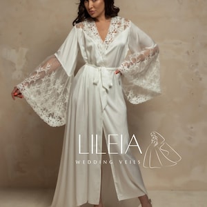 May include: A white satin wedding robe with lace sleeves and neckline. The robe has a tie waist and a long, flowing design. The text "LILEIA WEDDING VEILS" is printed on the robe.