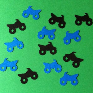 Puede incluir: Una colecci&oacute;n de recortes de papel azul y negro de veh&iacute;culos de cuatro ruedas, que se asemejan a quads o motocicletas todoterreno. Los recortes est&aacute;n esparcidos sobre un fondo verde.