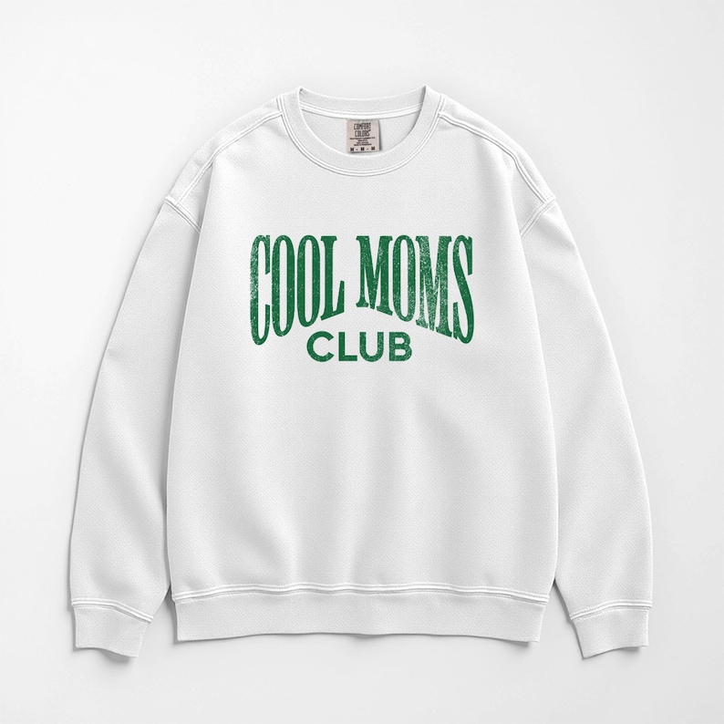 May include: White crew neck sweatshirt with the text "COOL MOMS CLUB" in distressed green lettering. The sweatshirt has a classic, casual style, perfect for everyday wear. The design is centered on the front.