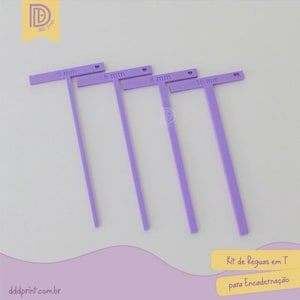May include: Four purple T-shaped rulers with measurements of 5 mm, 6 mm, 8 mm, and 10 mm. The rulers are arranged diagonally on a light background. Text on the image reads "Kit de Réguas em T para Encadernação".