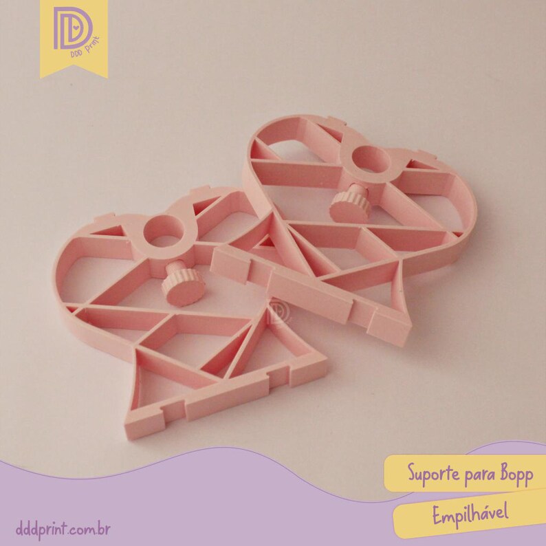 May include: Two light pink, heart-shaped plastic supports with geometric designs. Each has a central circular opening and a screw-like knob. The supports are designed to be stackable, as indicated by the text on the image.
