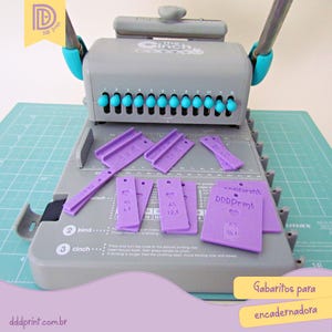 以下が含まれることがあります： 水色のアクセントが付いたグレーの The Cinch 製本機と、紫色の製本テンプレートのセット。テンプレートにはテキストとハート型の切り抜きがあります。「DDDprint.com.br」というテキストも表示されています。