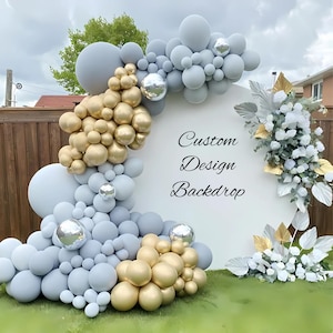 May include: A custom design backdrop featuring a white circular frame adorned with clusters of grey and gold balloons, silver accents, and floral arrangements. The backdrop has the words "Custom Design Backdrop" in elegant script.