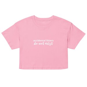 May include: A light pink crop top with short sleeves. The text "accidental litters do not exist" is printed in white across the front. The shirt is made of a soft, comfortable material.