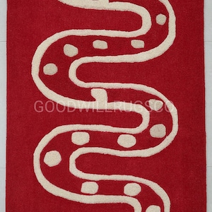 Peut inclure: Un tapis rectangulaire rouge avec un motif de serpent blanc. Le serpent sinueux présente des taches blanches et une tête détaillée. Le tapis est en matière douce et moelleuse, idéal pour une chambre ou un salon. Le tapis a le texte "GOODWILLRUGS".