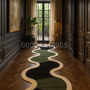 Può includere: Un tappeto astratto dal design fluido e organico. Il tappeto presenta una forma ondulata con sezioni nere, verde oliva e beige. È posizionato su un pavimento in legno scuro in un corridoio.