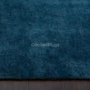 May include: A close-up of a teal-colored rug with a plush, textured surface. The rug is a solid color and appears to be made of a soft material. The text "GoodwillRugs" is visible in the lower right corner.