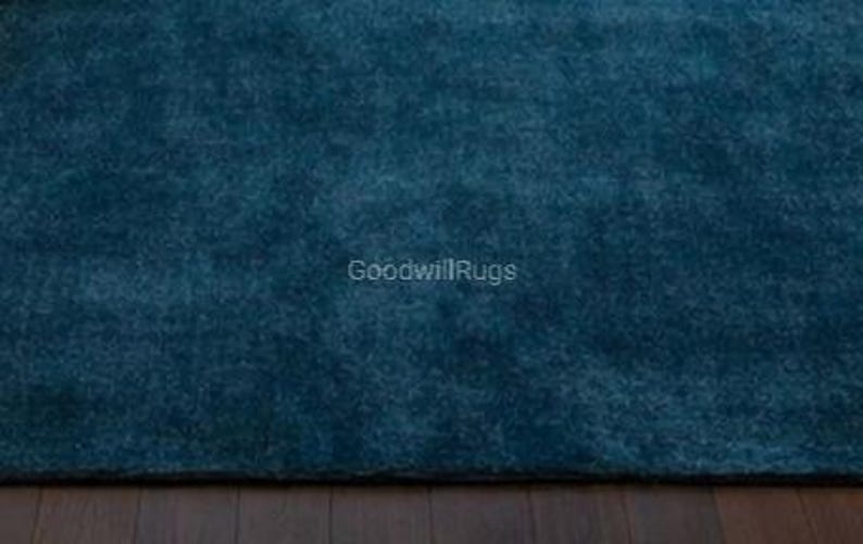 May include: A close-up of a teal-colored rug with a plush, textured surface. The rug is a solid color and appears to be made of a soft material. The text "GoodwillRugs" is visible in the lower right corner.