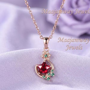 May include: Rose gold necklace with a pendant featuring a red star and crescent moon design, accented with green and clear gemstones. The chain and pendant are displayed against a soft purple background. The text "Maajamway Jewels" is visible.