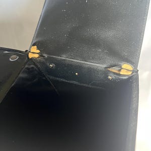 May include: Black leatherette box with visible wear and tear. The box has a hinged lid and shows signs of damage at the corners, with exposed yellow material. The interior of the box is black and appears empty.