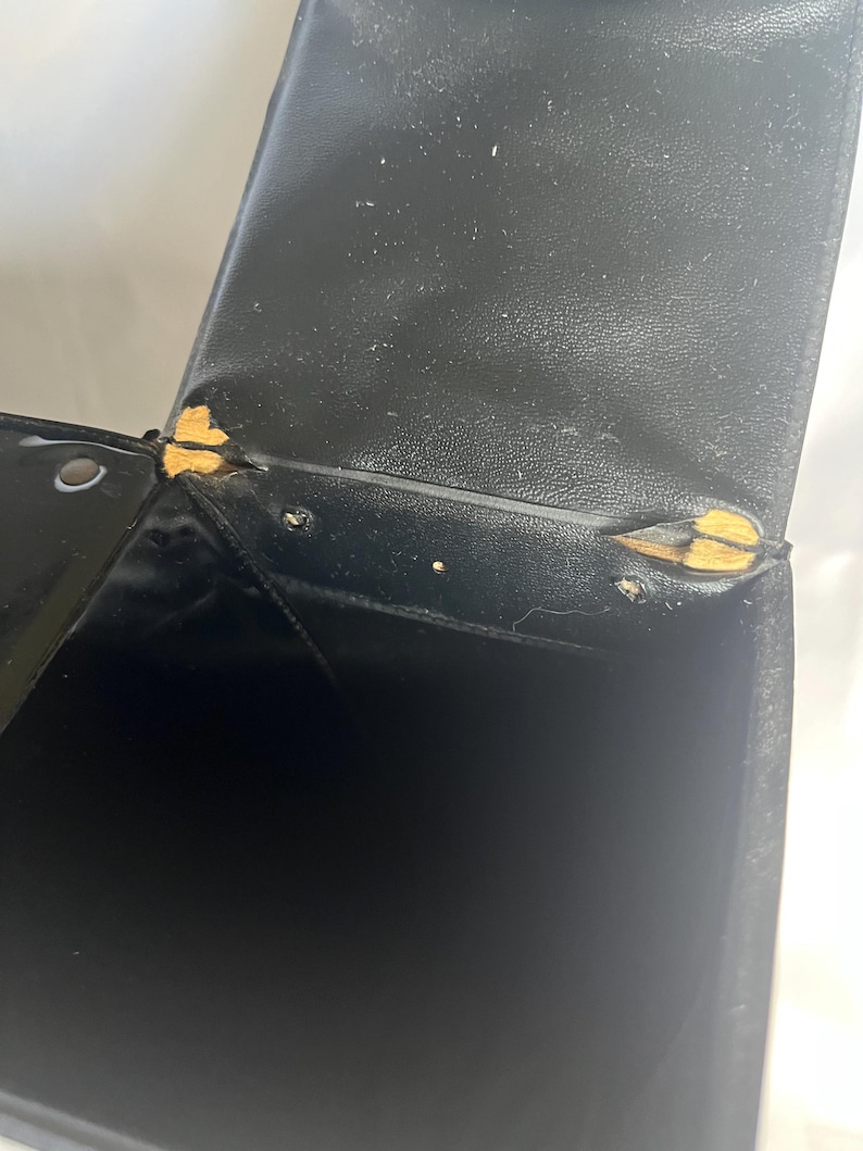 May include: Black leatherette box with visible wear and tear. The box has a hinged lid and shows signs of damage at the corners, with exposed yellow material. The interior of the box is black and appears empty.