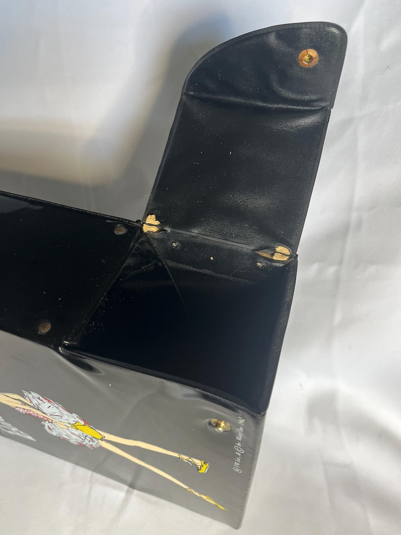 May include: Black vintage box with a hinged lid and a clasp. The box has a glossy finish and a decorative illustration of a woman in a dress. The lid is open, revealing the interior. The box is likely made of a hard material.