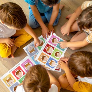 Puede incluir: Niños jugando con tarjetas de emociones. Cada tarjeta presenta una emoción diferente, como "alegría", "ira" y "sorpresa", con ilustraciones correspondientes. El texto "LOTERIA DE LAS EMOCIONES" es visible en las tarjetas.