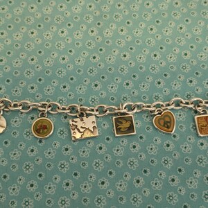 May include: Silver charm bracelet with various charms, including a dove, a peace sign, and a world map. The bracelet has a lobster clasp closure and a price tag that reads "PEACE CHARMS". The charms are in various shapes and colors.