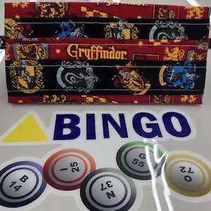 May include: A fabric wallet with a repeating pattern of crests and the word "Gryffindor" in gold lettering. Below the wallet are bingo number stickers and a "BINGO" sticker.