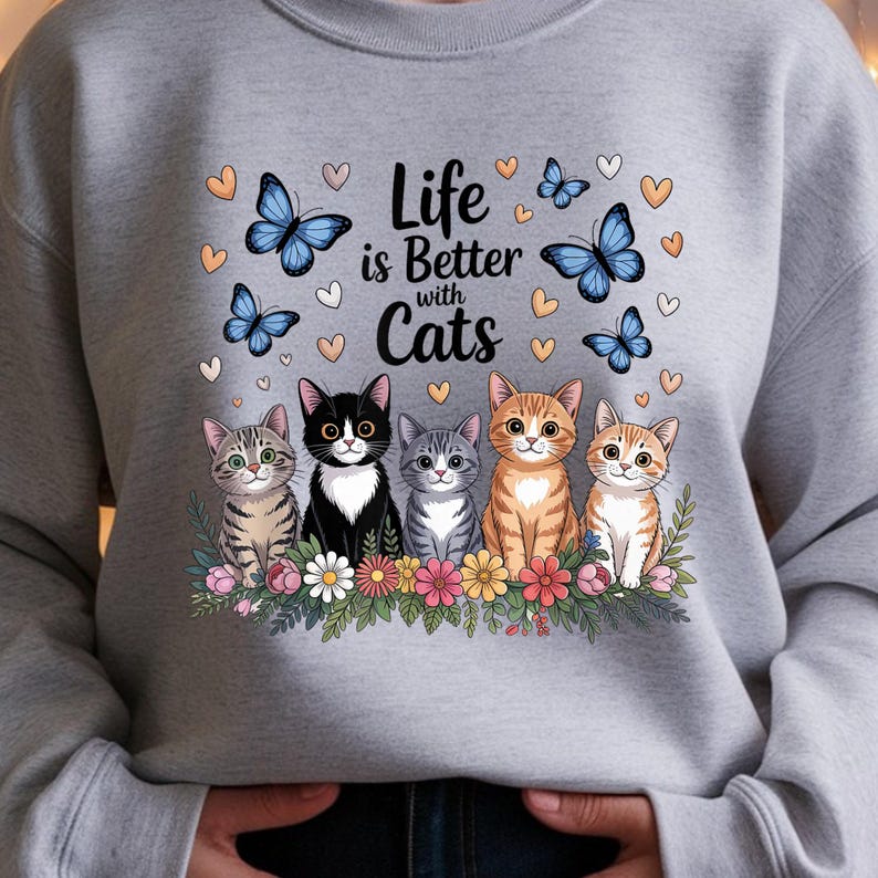 May include: A gray sweatshirt featuring the phrase "Life is Better with Cats" with five cartoon cats, butterflies, and hearts. The cats are various colors and patterns, sitting above a floral border.