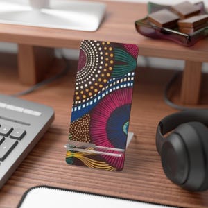 Könnte beinhalten: Ein vertikaler Telefonständer mit farbenfrohem afrikanischem Druckdesign. Der Ständer zeigt ein lebendiges Muster aus Kreisen und Linien in Pink-, Blau-, Gelb- und Grüntönen. Er besteht aus einem robusten Material und ist für ein Telefon konzipiert.