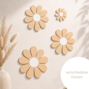 Könnte beinhalten: Vier Wanddekorationen in Blumenform in verschiedenen Größen, jeweils mit hellbeigen Blütenblättern um ein weißes, kreisförmiges Zentrum. Das Set besteht aus drei großen und einer kleineren Blume, die auf einer schlichten Fläche angebracht sind.
