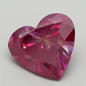 May include: A faceted, heart-shaped gemstone in a vibrant shade of pink. The gem's surface is cut with numerous facets, creating a play of light and shadow. The heart shape is clearly defined, with a polished, reflective surface.